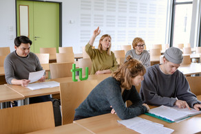 Students Hand Signal_09 Students in the seminar room are sitting at the tables. One of them is giving a hand signal.